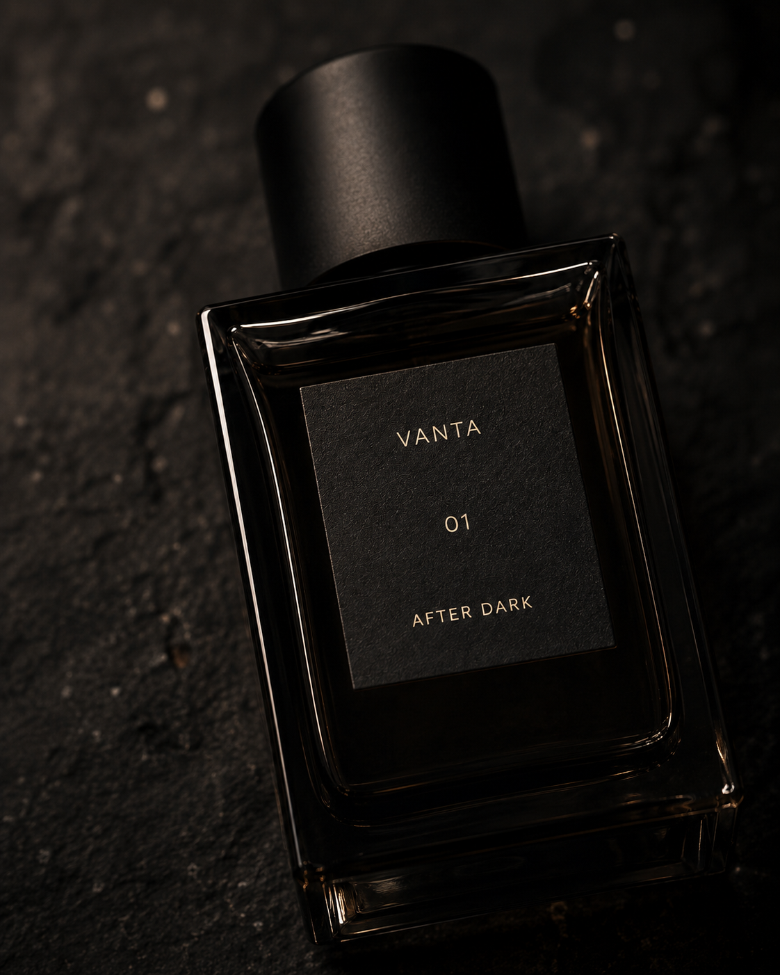 Close crop of the VANTA 01 bottle on rough dark stone, light raking across the heavy glass edges