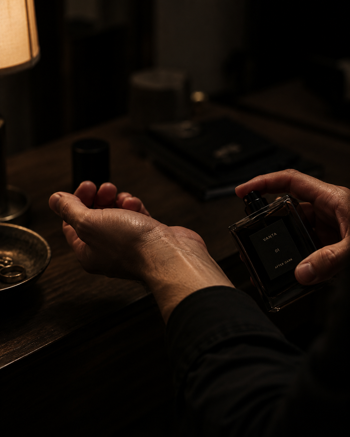Hands holding the VANTA bottle above a wrist at a dark wooden desk beside a low lamp
