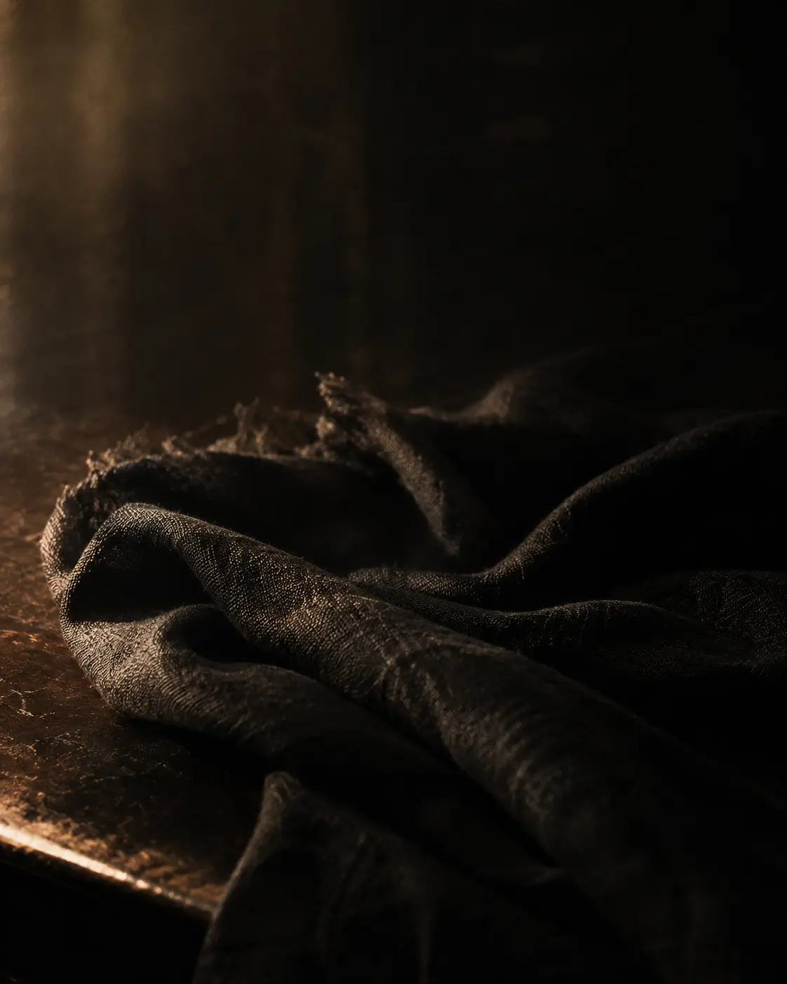 Dark linen fabric folded on a worn table, edged by low tungsten light
